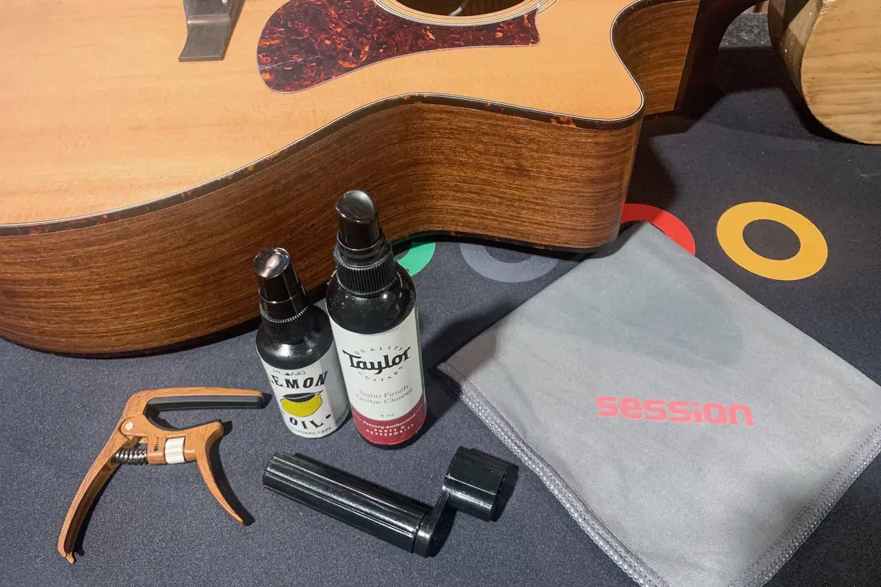 Gitarre reinigen: Zubehör wie Saitenwickler, Kapodaster und Pflegeprodukte liegen neben einer Akustikgitarre.
