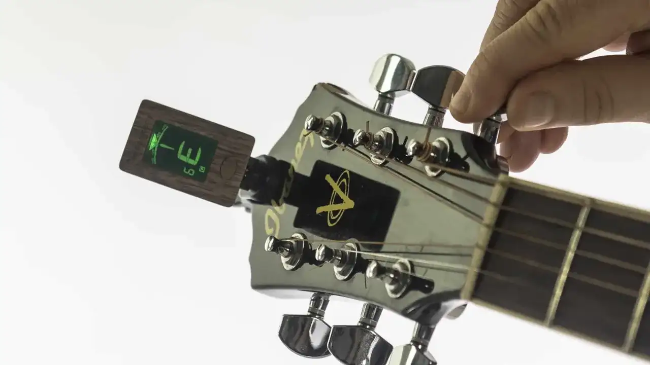 Eine Hand stimmt die Gitarre mit einem Clip-Tuner. Der Tuner zeigt "E" an, was bedeutet, dass die Saite perfekt gestimmt ist.