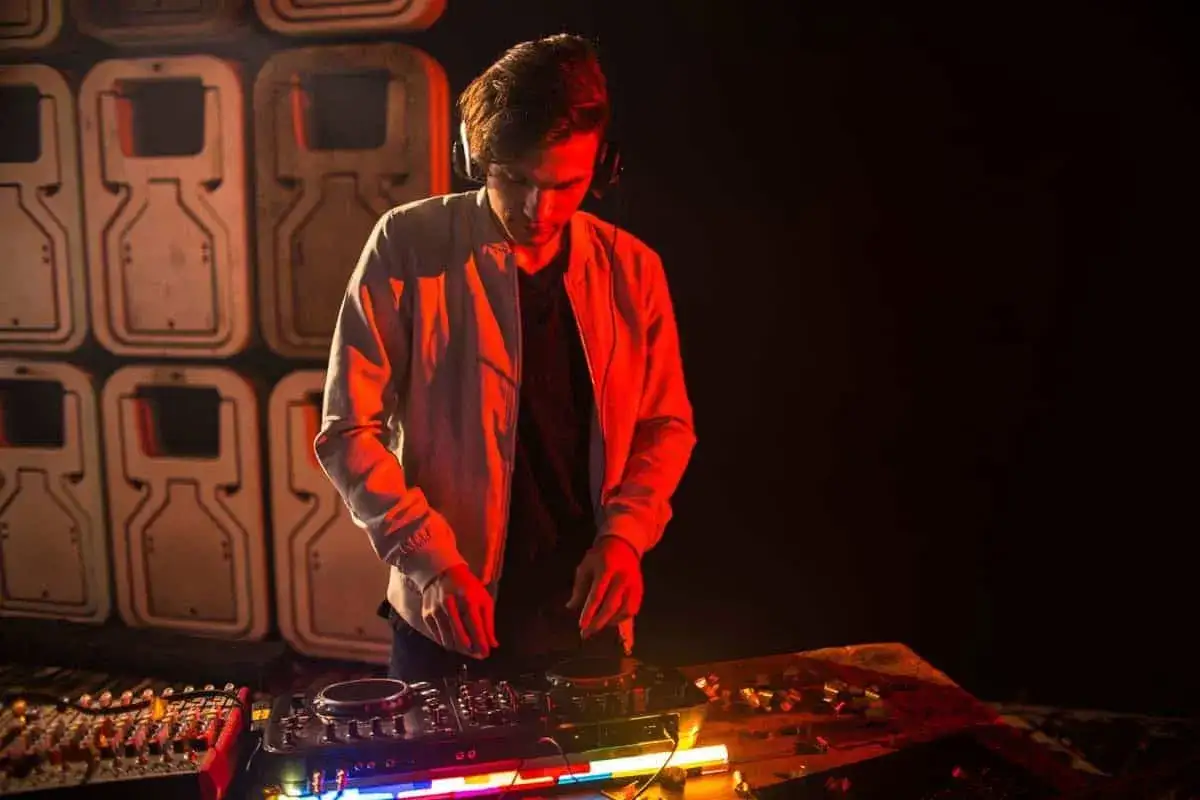 Ein guter DJ mit Kopfhörern legt Musik auf, beleuchtet von rotem Licht. Im Hintergrund sind Lautsprecher zu sehen.