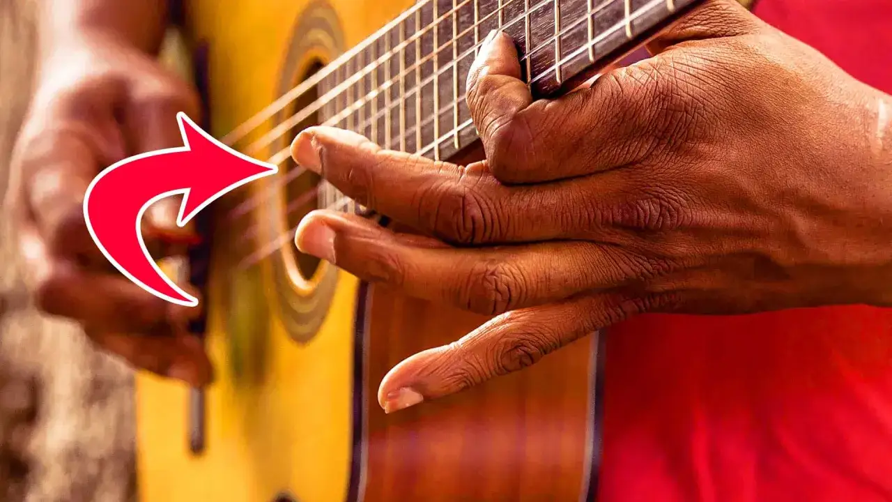 Nahaufnahme einer Hand, die eine Gitarre im Fingerstyle spielt. Die Finger greifen die Saiten, während ein roter Pfeil auf die Technik hinweist.