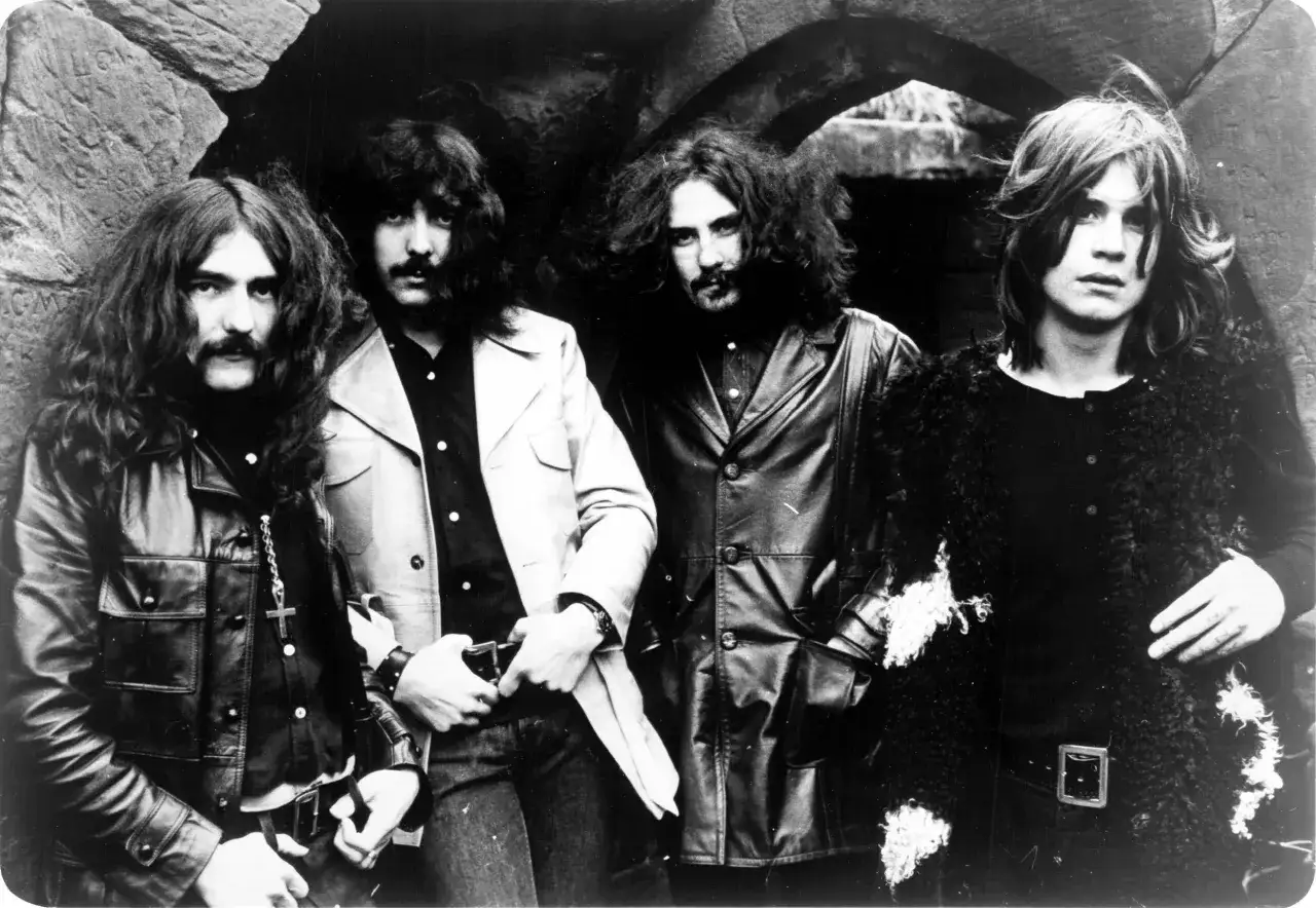 Vier M&auml;nner mit langen Haaren und Schnurrb&auml;rten, die wie die erste Metal Band aussehen, posieren vor einem steinernen Torbogen.
