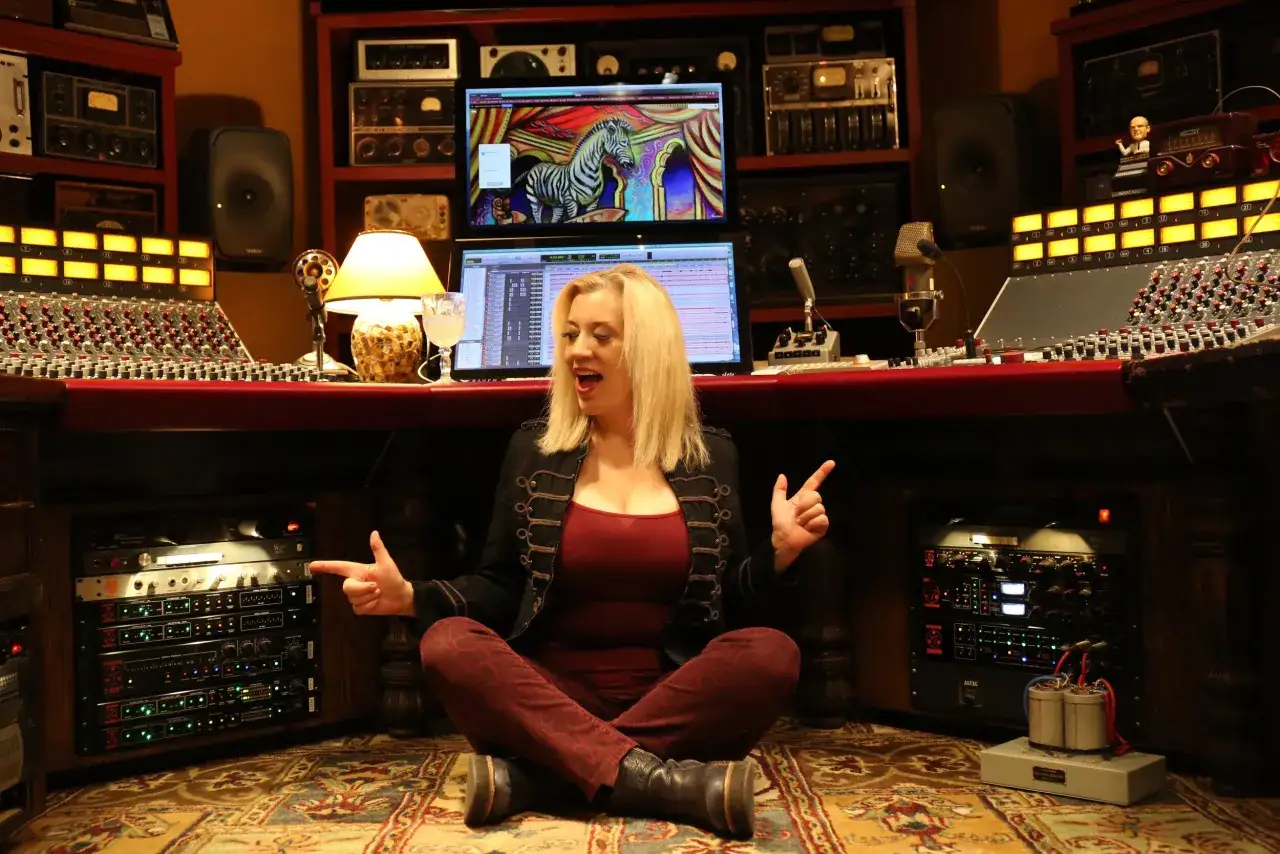 Sylvia Massy sitzt im Schneidersitz vor einem Mischpult, umgeben von Studio-Equipment.