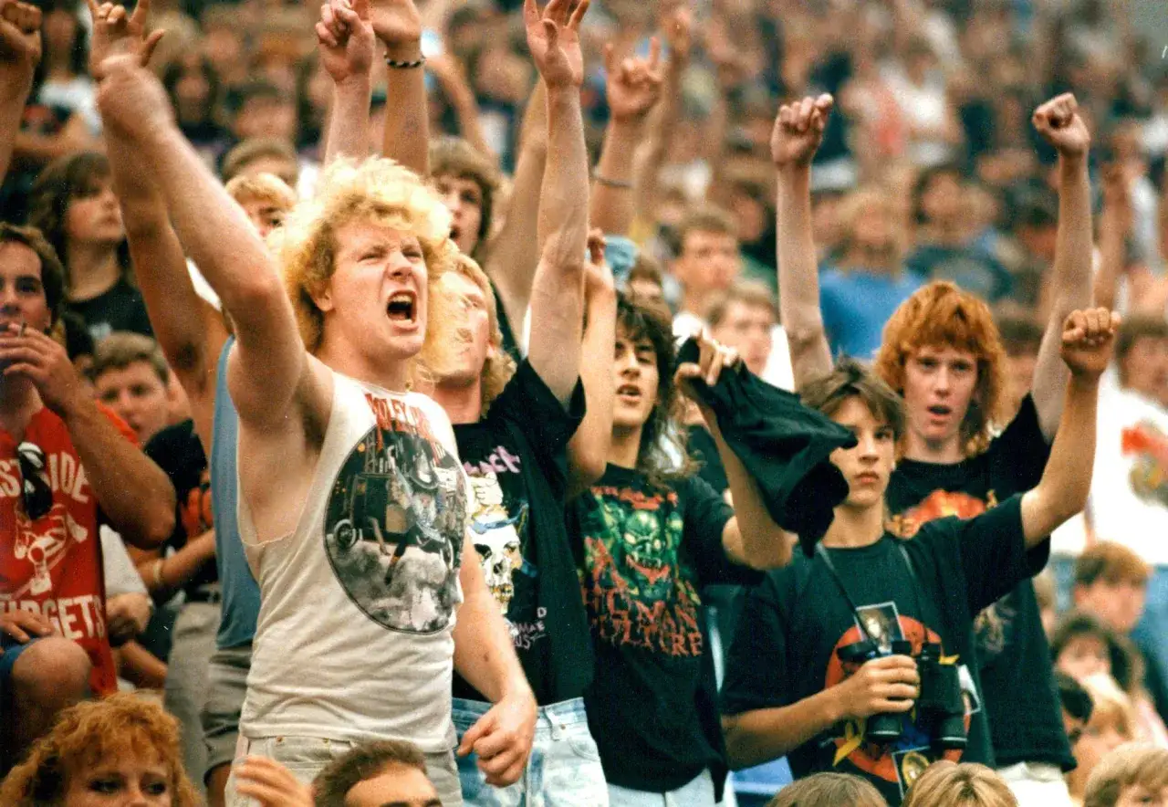 Fans jubeln bei einem Konzert der metal bands 80er. Sie tragen Band-T-Shirts und machen das 