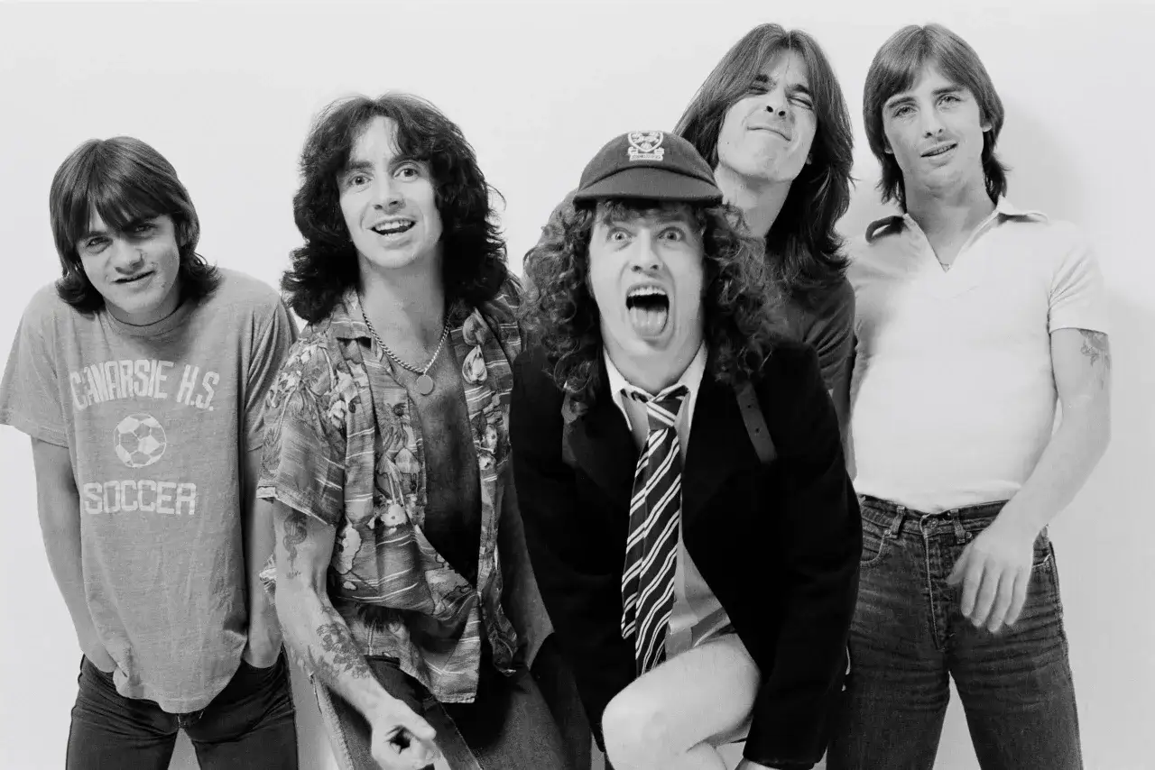 Fünf junge Männer, darunter die Malcolm Young Geschwister, posieren für ein Foto. Einer trägt ein T-Shirt mit