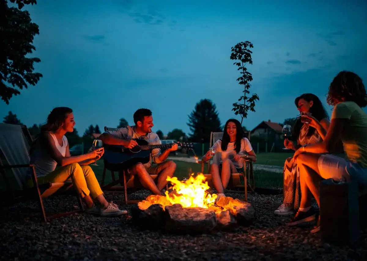 Freunde singen Lagerfeuer Lieder zum Mitsingen, während einer am Lagerfeuer Gitarre spielt.