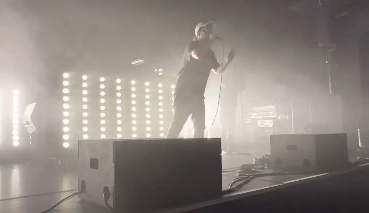 Ein Mann mit Mikrofon auf einer B&uuml;hne, umgeben von Nebel und Lichtern. Er k&ouml;nnte der beste deutsche Rapper sein, der gerade sein Publikum begeistert.
