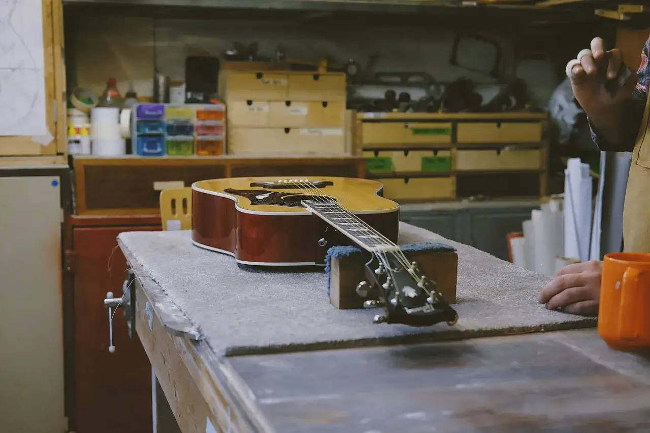 Eine Akustikgitarre liegt auf einer Werkbank, bereit für die Gitarre reinigen. Werkzeuge und Zubehör sind im Hintergrund zu sehen.