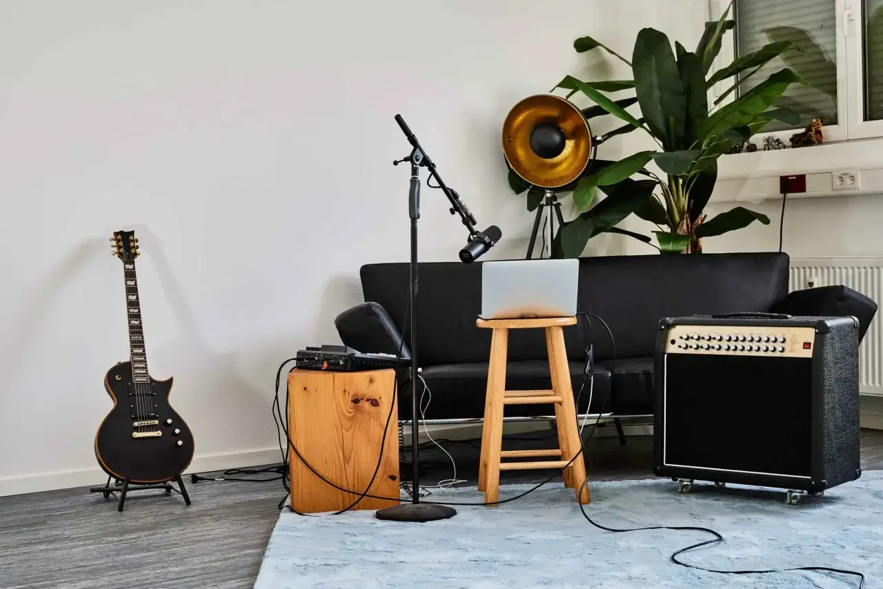 Schwarze E-Gitarre, Mikrofon, Verstärker und ein Laptop auf einem Hocker – bereit, die Gitarre aufzunehmen und am PC zu bearbeiten.