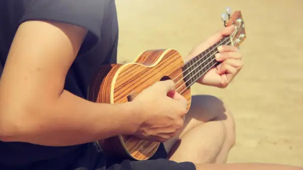 Person spielt auf einer Ukulele, die Hände formen den D-Dur-Akkord. Die Holzmuster der Ukulele sind gut sichtbar.