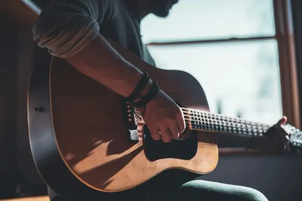 Mann spielt Akustikgitarre, Schatten fallen auf das Holz. Informiere dich über die Gitarrenunterricht Kosten, um deine musikalischen Träume zu verwirklichen.