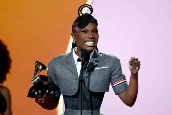 Glückliche schwarze Rapperin mit Grammy-Trophäe und einzigartiger Frisur, die auf der Bühne jubelt.