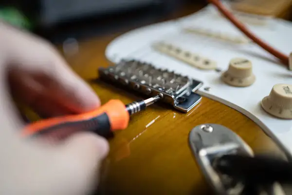 Hand mit Schraubendreher stellt die Gitarre ein.