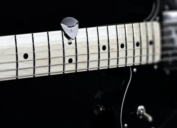 Nahaufnahme eines Plektrums auf den Saiten einer Gitarre. Perfekt, um die **Gitarre Saitenlage einstellen** zu lernen.