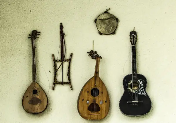Alte Saiteninstrumente hängen an der Wand. Eine schwarze Gitarre, eine birnenförmige Laute und zwei weitere, wie sie die erste Gitarre aussehen ließen.