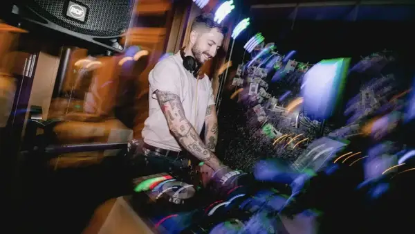 Ein guter DJ mit tätowierten Armen legt Musik auf, während bunte Lichter die Szene in Bewegung setzen.