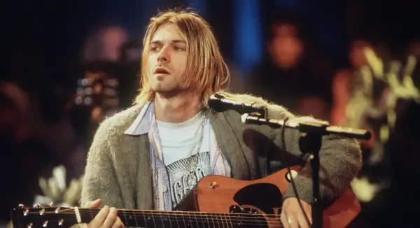 Kurt Cobain spielt Akustikgitarre, ein ikonisches Bild, das an eine verstorbene Rockmusiker Liste erinnert.