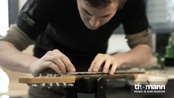 Ein Mann arbeitet an der bund gitarre. Er justiert die Saiten mit seinen Fingern.