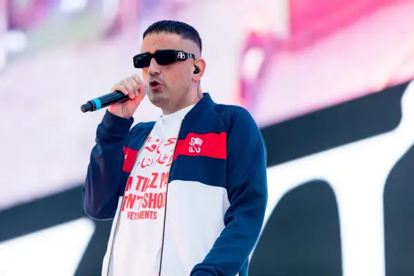 Der beste deutsche Rapper mit Mikrofon auf der Bühne, trägt Sonnenbrille und Bomberjacke.