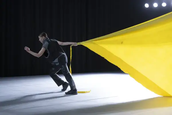 Tänzerin zieht ein gelbes Tuch, das sich wie ein Segel im Wind kräuselt. Perfekt für gute Lieder zum Tanzen Choreographie.