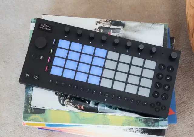 Ein schwarzes Ableton-Controller-Pad mit leuchtenden blauen Pads liegt auf gestapelten Büchern. Perfekt für jeden, der Musik machen will und den "ableton move" liebt.