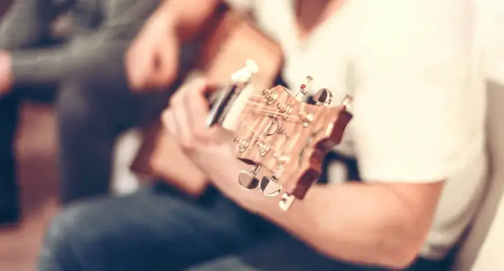 Nahaufnahme einer **bending Gitarre**, die von einer Person gespielt wird. Der Fokus liegt auf dem Hals und den Stimmmechaniken.